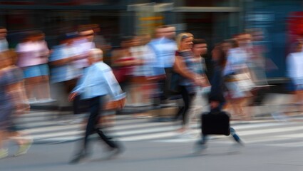 Blurred motion of pedestrians crossing a city street on a sunny day