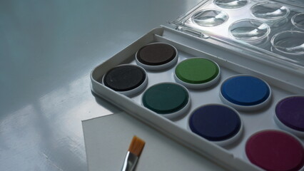Watercolor paints in a box on a white table with a brush