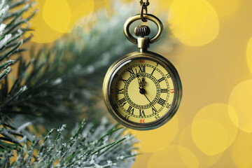 Pocket watch and fir tree branches against golden background with blurred lights, closeup. New Year...