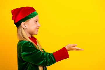 Smiling child in a festive elf costume poses against a vibrant yellow background, ready to spread...