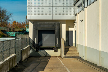 Loading dock at a commercial building. Closed gate and concrete stairs leading to an entrance. Detail of logistic service area and delivery zone.
