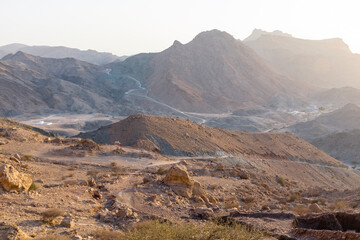 Scenic view from khoneh Mountain in Oman during sunset, showing rocky ridges, desert valleys, and the surrounding town bathed in golden light.