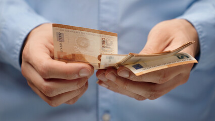 Close-up of male hands counting euro banknotes. Man in blue shirt holds European currency....