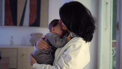 Mother holding baby close to chest, comforting and rocking child as he calms down after crying, tender moment of affection in warm evening home light - Powered by Adobe
