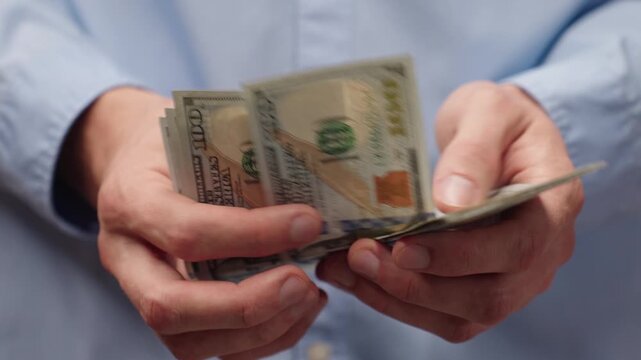 Close-up of male hands counting US dollar bills. Man in blue shirt counting money, 100 dollar banknotes. Financial concept background for income, salary or savings planning.