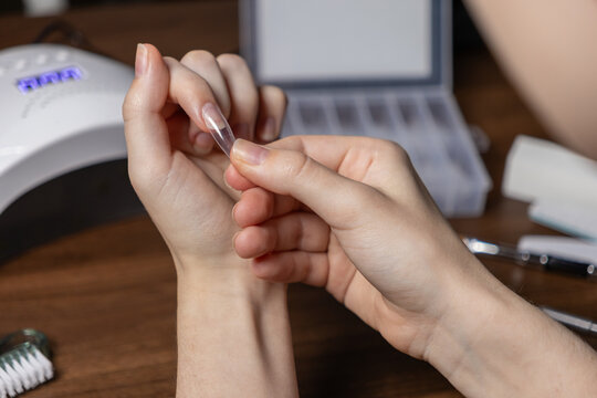 Woman applying clear nail extension upper form on her finger for a DIY manicure at home, symbolizing self-care and beauty routine