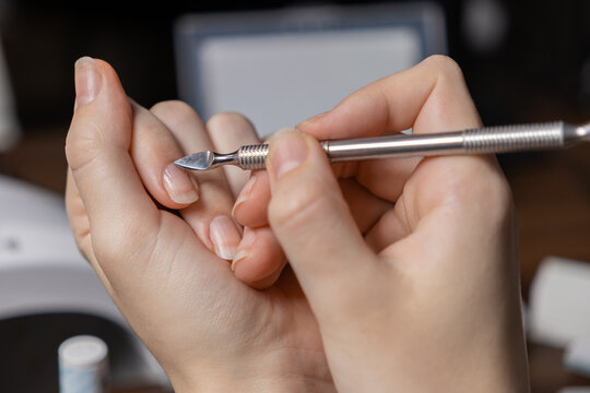 Close-up of a person performing a meticulous personal manicure by oneself, using a metal cuticle pusher tool for precise natural nail care, promoting hygiene and a wellness beauty routine