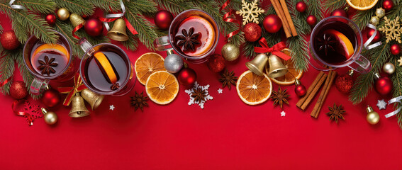 Christmas composition with mulled wine, fir branches, dried oranges, spices and festive decorations on red background. Warm holiday concept.