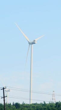 White wind turbine stands in middle of vast green field. Enormous windmill rotates blades in wind and produces clean electricity. Vertical shot