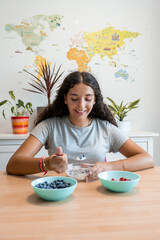 Smiling young woman eating yogurt with fresh berries at home