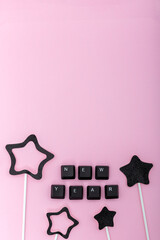 Word new year made of keyboard keys surrounded by black paper stars on pastel pink background. Concept of digital holiday greeting, online celebration and creative modern minimalism. Vertical photo