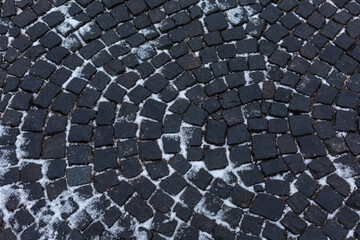A dirty gray cobblestone road with snow. Winter and urban architecture. Background. Space for text.
