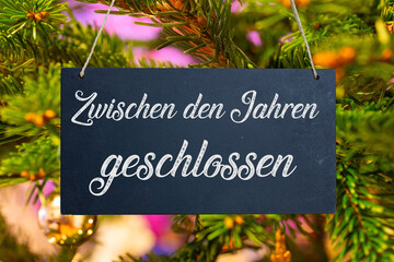 Betriebsferien an Weihnachten: Schild mit der Aufschrift ZWISCHEN DEN JAHREN GESCHLOSSEN vor einem Weihnachtsbaum