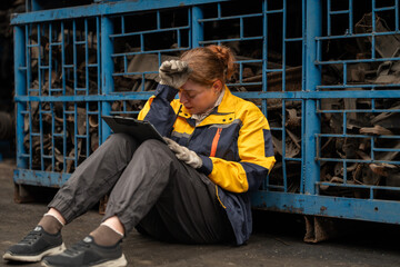 Exhausted female warehouse worker with cardboard sitting in warehouse factory under stress. Stressed woman mechanic sitting in auto workshop with serious concern