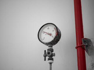 Pressure gauge with red pipe against a plain gray wall