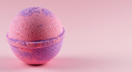 Single pink and purple bath bomb on solid pink background. Handmade cosmetic product for spa and self-care. Banner with copy space for text