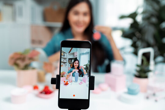 Selective focus smartphone with young beautiful Asian reviewing cosmetic makeup brush cheek test collection with pastel color, showing glow blusher mood to promote on social media online. Stratagem.