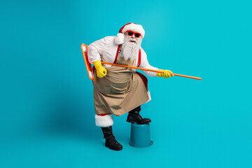 Santa in apron and hat with yellow gloves posing on a stool holding a long orange pole for a...