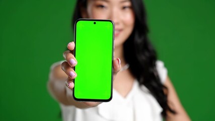 Beautiful asian woman showcasing smartphone with green screen against chroma key background offering digital promotion and business advertising - Powered by Adobe