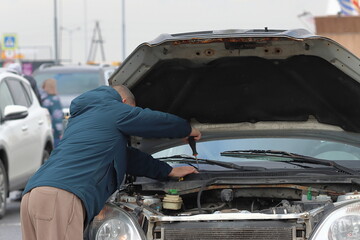 A man performs minor repairs on an old car. A driver repairs a passenger car