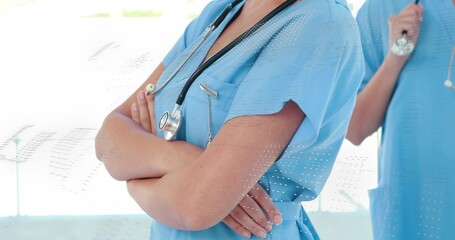 Standing nurse in scrubs crossing arms, colleague holding stethoscope in hospital hallway, sunlight