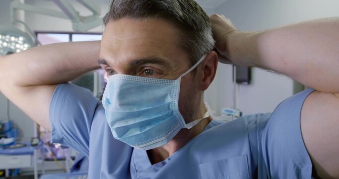 Securing surgical mask straps male surgeon preparing in operating room, with light and monitor - Powered by Adobe