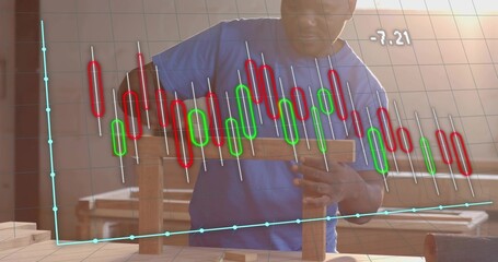 Man wearing blue t-shirt building wooden blocks in workshop by windows, candlestick chart overlay