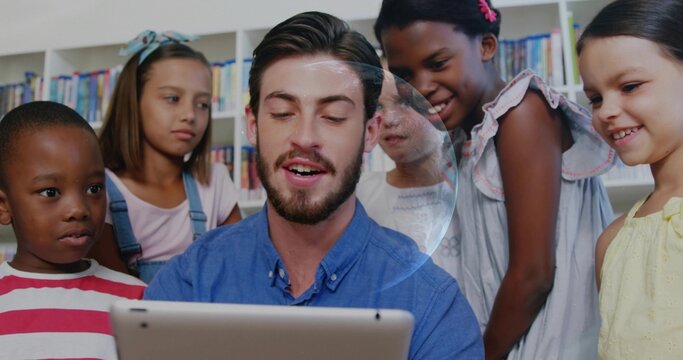 Holding tablet teacher in blue shirt leading storytime with five children in library, with books