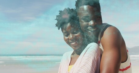 Hugging adult couple wearing pink striped shirt and white tank top on sandy ocean edge