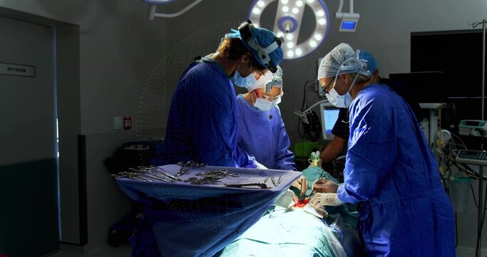 Surgical team wearing blue scrubs performing surgery under surgical light, with instrument tray