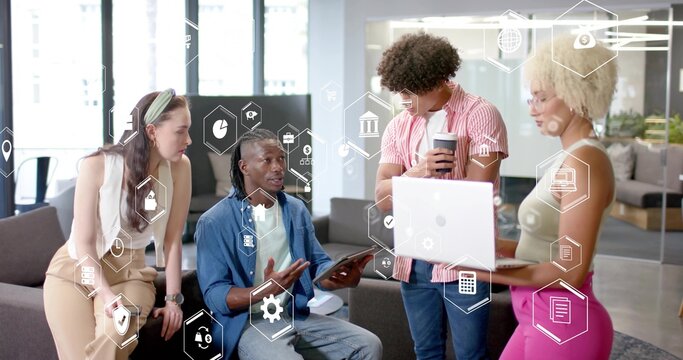 Collaborating team holding tablet and laptop in open office lounge, with floating digital icons