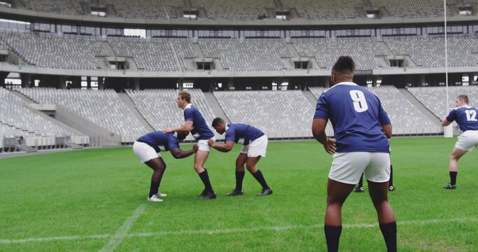 Practicing rugby players wearing navy jerseys forming scrum on grass pitch, with goalpost