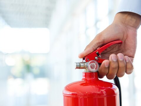 Hand holding a red fire extinguisher, ready for emergency use - Powered by Adobe