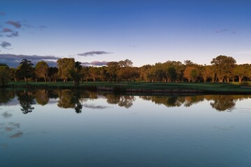 Obraz premium Serene lake scene at sunset with reflections of trees and a calm sky creating a peaceful atmosphere