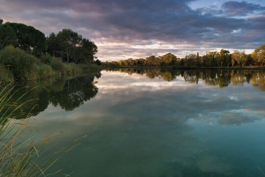 Tranquil lake reflecting colorful clouds under evening sky surrounded by lush greenery