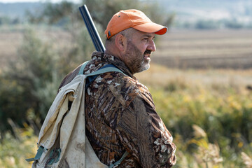A hunter with a gun in camouflage clothing. A senior man with a gun, medium shot, searching for game.