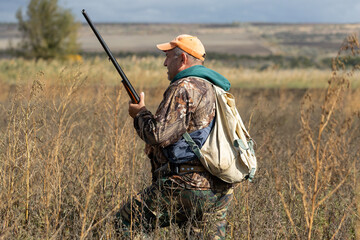 A hunter with a gun in camouflage clothing. A senior man with a gun, medium shot, searching for game.