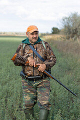 A hunter with a gun in camouflage clothing. A senior man with a gun, medium shot, searching for game.