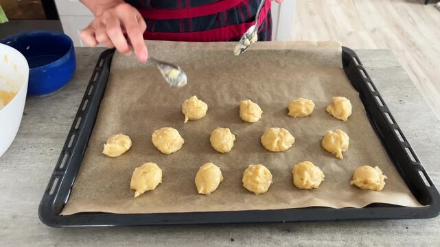 4K video of female hands putting cookies dought using spoon on baking tray covered baking paper in home kitchen. Healthy food, people work or cozy home concept footage.