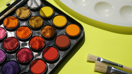 Palette of watercolors and paint brushes on a green background