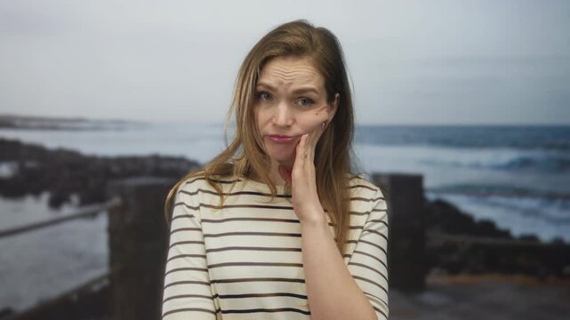 Young caucasian woman touching cheek on quiet street with pained expression and bare cheek visible; toothache pain.