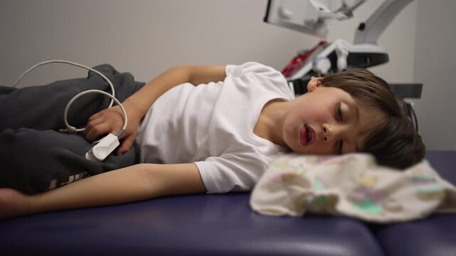 Young boy lying in hospital bed struggling to breathe during asthma attack, oxygen monitor on finger as he rests in exhaustion, emotional moment of vulnerability and medical care