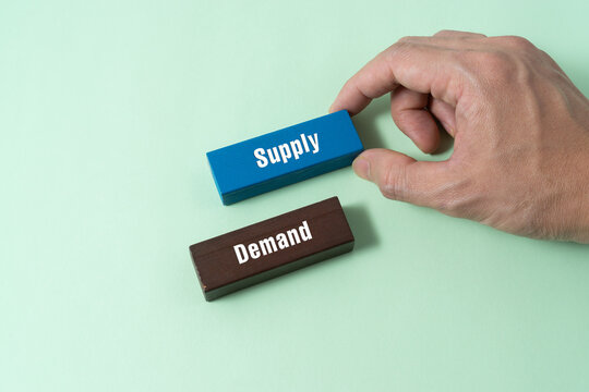 Supply and demand concept with human hand holding wooden block
