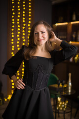 A woman in a black dress and stockings stands in front of a Christmas tree. She smiles and poses for the camera. The concept of holidays and Christmas.