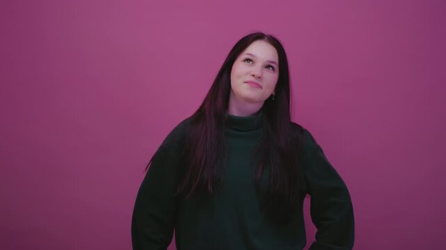 Close up portrait: Caucasian teenage girl in a pink studio in green sweatshirt is lost in thought, looking up. Young brunette woman reflects, creates thoughts. Beautiful female, generation Z or alpha