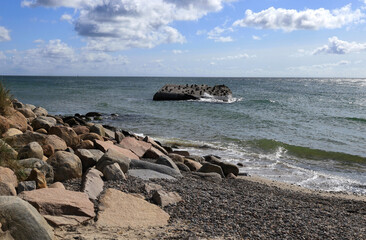 Landscape photo with a view of the Baltic Sea coast with large rocks and pebbles and a stone in the sea with birds sitting on it at Cape Grenen, in Skagen, northern Denmark