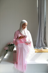 An Islamic woman in a pink dress drinking tea	
