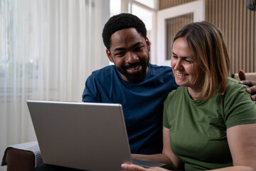 Cheerful diverse loving young couple using laptop and analyzing finances.