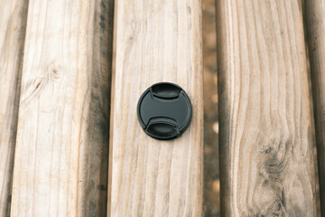 Camera lens cap on a wooden bench, close-up of photography accessory outdoors