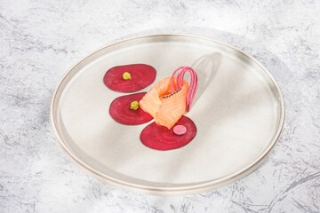 A delicate arrangement features rolled salmon, beetroot circles adorned with green dots, and pink flourish. This culinary creation sits on a contemporary plate